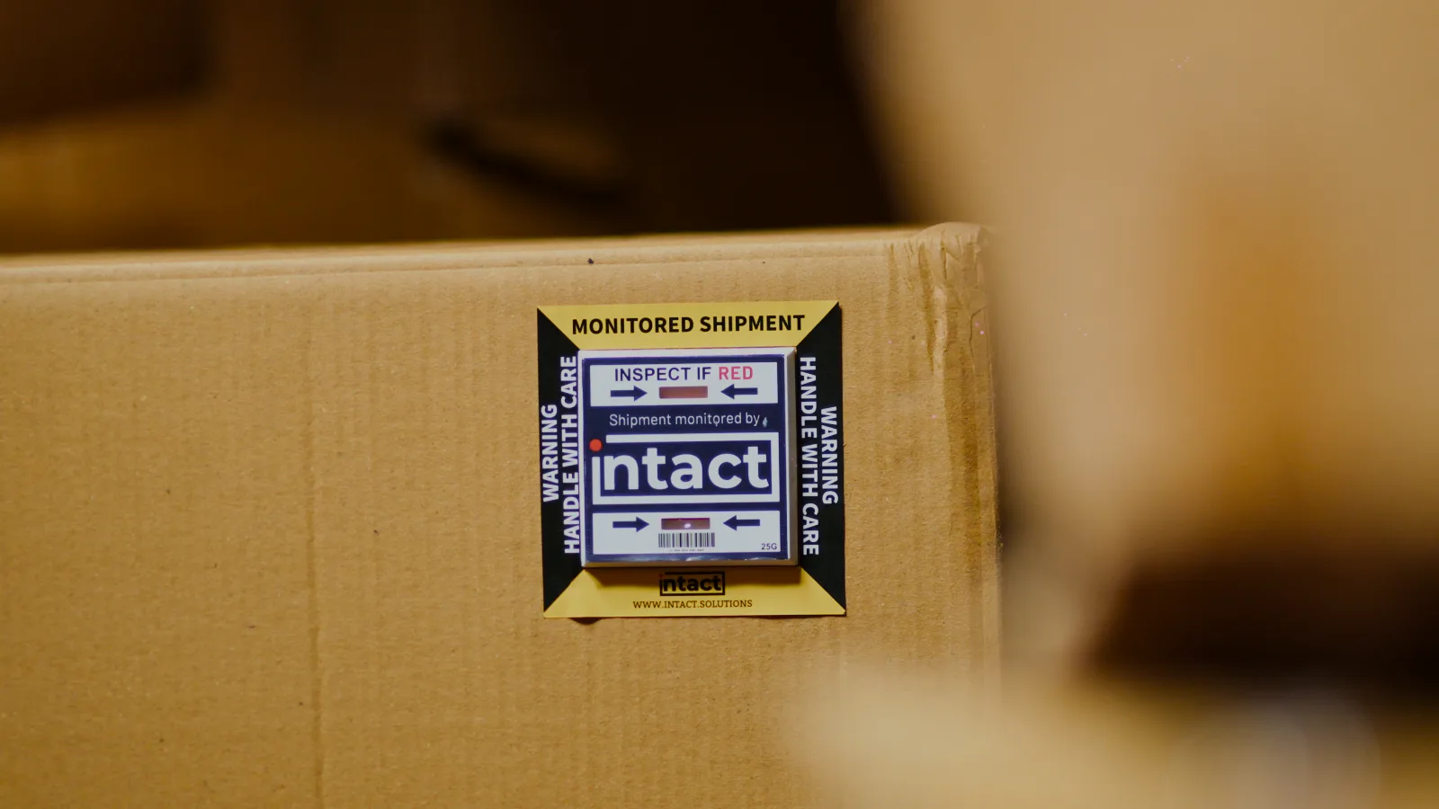 An iNTACT impact indicator in a yellow and black Monitored Shipment label on a carton.